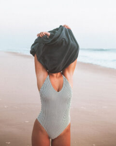 Mujer en bañador quitándose la camiseta en la playa en verano.